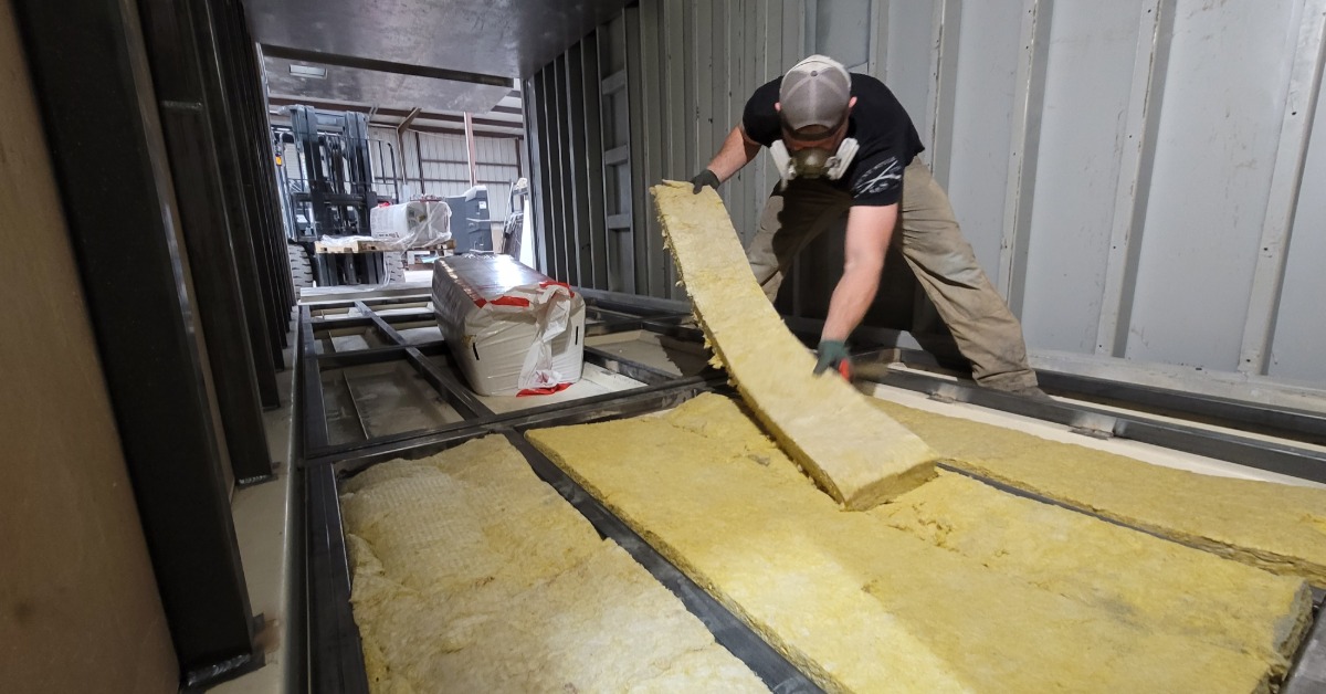 A worker wearing a safety gas mask installing insulation foam into storage building on a construction site.