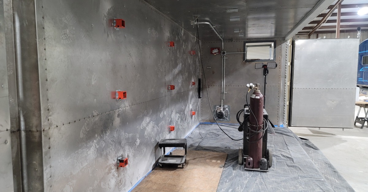 The interior of a flammable storage building. A thick steel wall is in place with a canister of pressurized gas nearby.