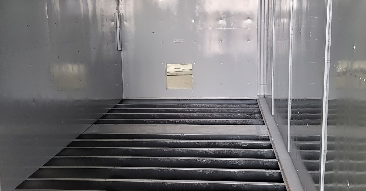 The interior of a large shipping container. The floor of the container is not in place, revealing bare metal.