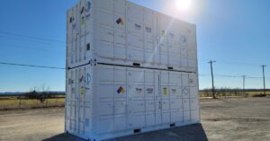 Two large, white storage containers stacked on top of each other in an open parking lot with grass behind it.