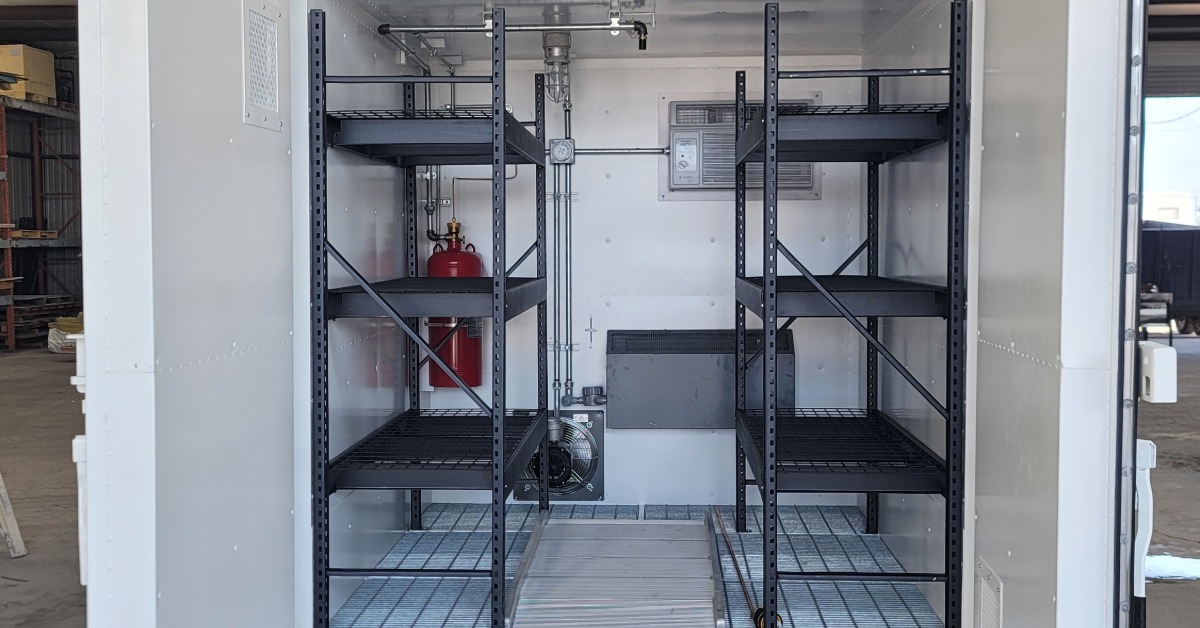A white storage container with its side doors open. There are sets of black shelving units inside the container.