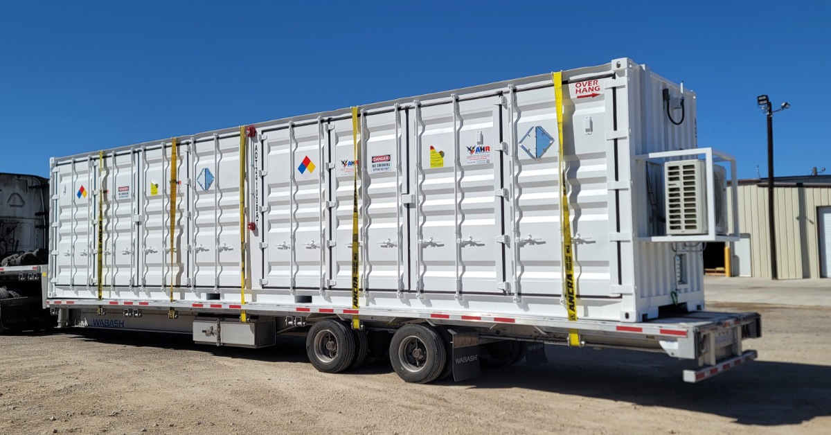A large, white storage container on the bed of a semi-truck. The side of the container has multiple warning stickers.