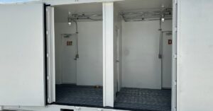 The side of a white storage container with its side doors wide open. There are exit doors in to the back of the containers.
