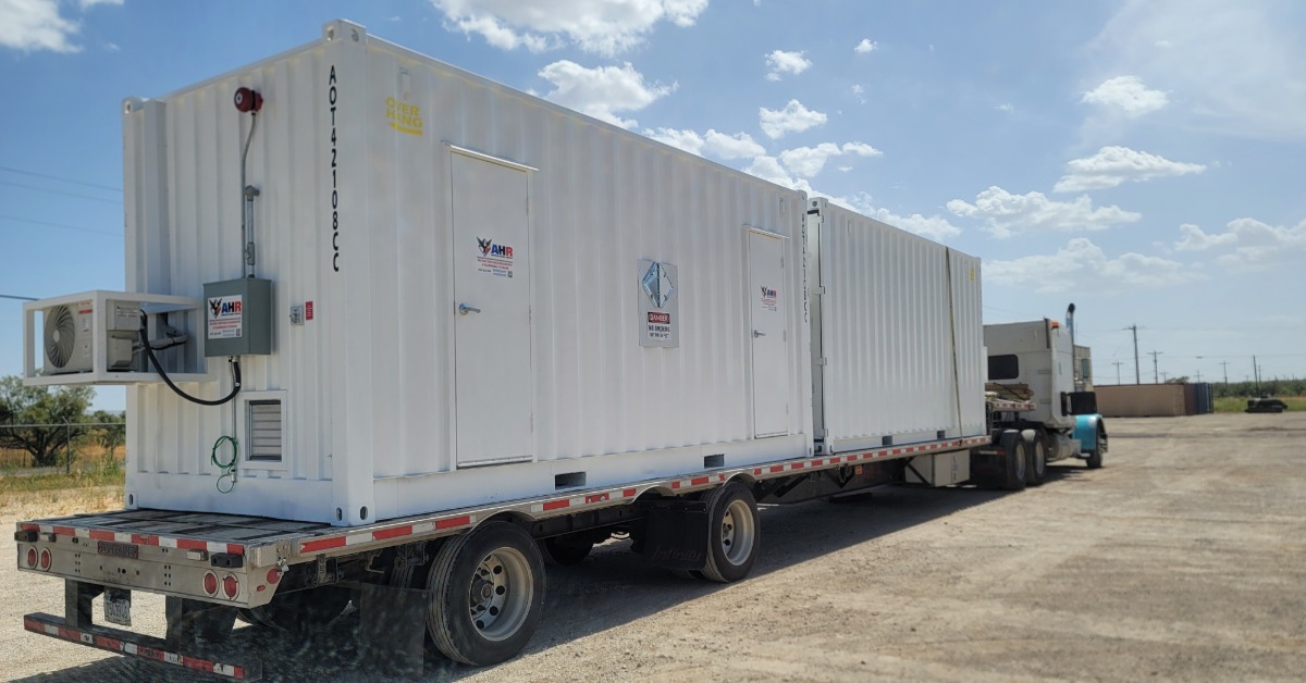 A large, white storage container placed on the bed of a truck. There is a small air conditioning unit on the container.