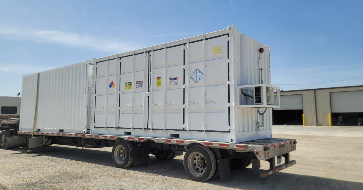 A large, white storage container place on the back of truck. The container has multiple warning labels on its side.